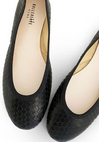 Ballerines noires avec des écailles texturées et en relief. Bout arrondi, bord élastiqué et doublure intérieure beige. Nom de la marque visible à l'intérieur.
