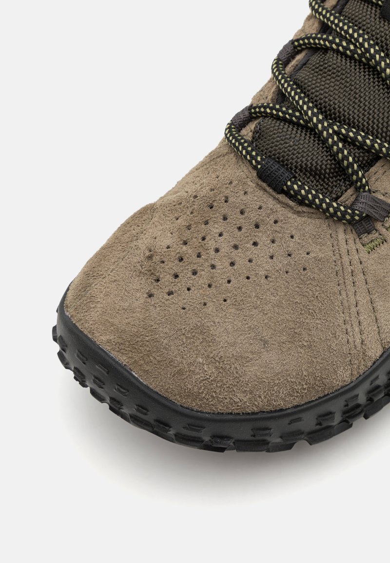 Bruine suède schoen met een gestructureerde bovenkant, zwarte rubberen zool en patroonveters. Heeft perforaties bij de neus voor ademend vermogen.