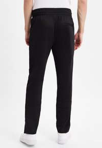 Schwarze Sporthose mit elastischem Bund, schmal zulaufenden Beinen und horizontalen Nähten unter den Knien, kombiniert mit weißen Sneakern.