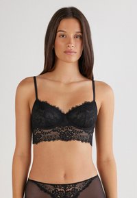 Zwarte kanten bralette met verstelbare dunne banden, scalloped randen en bloemmotieven. Het gelaagde ontwerp heeft een cropped fit.
