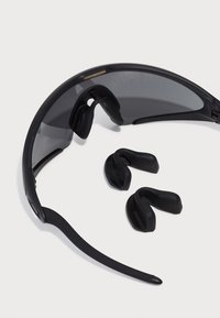 Occhiali da sole sportivi neri con lenti scure, supporti per le orecchie flessibili e un design aerodinamico. Include pezzi aggiuntivi in gomma nera per le orecchie.