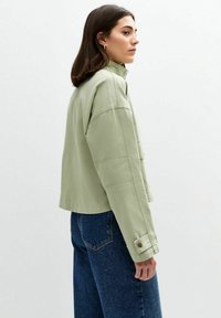 Ljusgrön kort jacka med hög krage, med vida ärmar och knäppte manschetter. Matcher med mörkblå denim.