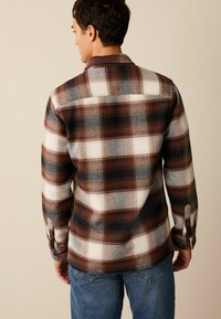 Brun og hvidternet flannel skjorte med krave, knapmanchetter og struktureret stof. Båret over blå jeans, set fra ryggen.
