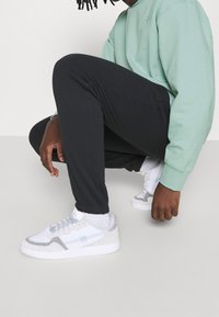 Svarta byxor, ljusgrön sweatshirt och vita sneakers med grå accenter. Byxorna har en slim fit och ribbad mudd. Sneakers har en strukturerad design.