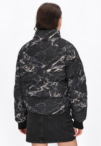 Pufferjack in zwart met een marmerpatroon van beige en grijze aderen. Kenmerkt zich door een hoge kraag en geribde manchet. Gekocht met een zwarte denimrok.