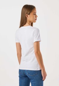 Hvid t-shirt med korte ærmer og rund hals, lavet af bomuld, kombineret med blå denimjeans. Pasformen er afslappet og struktureret.