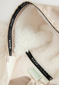 Beige jassenbinnenkant met zachte, witte nepbontvoering. Voorzien van een zwart label met "BAKER by Ted Baker" in het wit geborduurd. Glad stof.