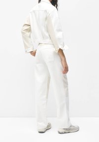 Biała dżinsowa kurtka i dopasowane spodnie, z kontrastowymi panelami, prostym krojem i widocznymi detalami ściegów. Casualowy styl z długimi rękawami.