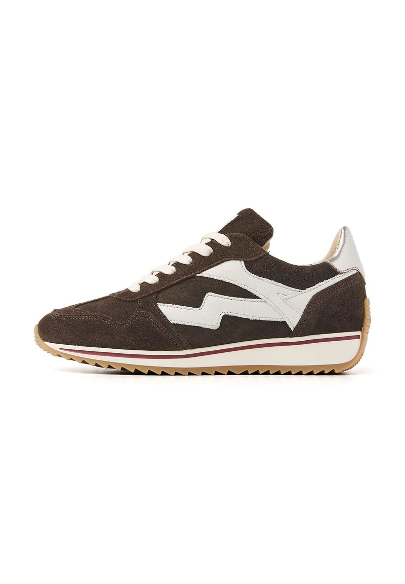 Sneaker en daim marron avec des accents blancs, présentant un design en zigzag, des lacets et une semelle en caoutchouc texturée avec une bande rouge contrastante.