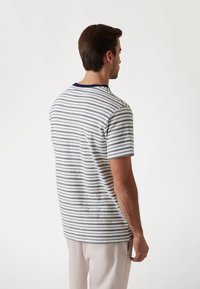 Camiseta de manga corta a rayas con rayas verticales en azul marino y blanco, con cuello redondo y un corte holgado, vista desde la parte posterior.