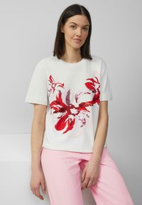 Weißes Baumwoll-T-Shirt mit rotem Blumenmuster. Gerader Schnitt mit kurzen Ärmeln, kombiniert mit hellrosa Hosen. Einfacher runder Ausschnitt.