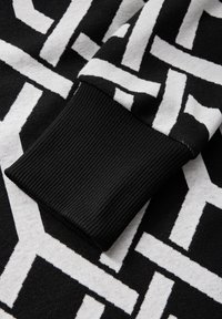 Stickad tröja med ett svartvitt geometriskt mönster; ribbad svart mudd; mjuk textur, medel tjocklek och kontrasterande färger.