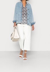 Jeansjacke, blumenbedruckte Bluse, weiße weit geschnittene Hose, Sandalen mit transparenten Riemen, hält eine Handtasche aus Creme mit strukturiertem Design und Akzenten.