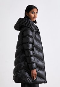Čierna pufferná bunda s prešívaným dizajnom, kapucňa s vertikálnym rebrovaním, predný zips a elastické manžety, ukazujúca lesklý materiál.