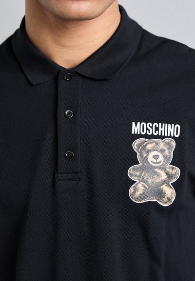 Black polo shirt featuring a textured fabric, three-button placket, and a graphic print of a teddy bear with the word "MOSCHINO" above it.