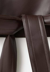 Prim-plan cu o curea din piele maro închis, cu cusături detaliate și o buclă care fixează capătul curelei pe un fundal alb.