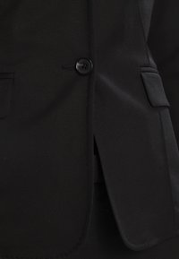 Černý blazer s texturovaným materiálem, s jedním knoflíkem a dvěma předními kapsami s klopami. Klasický střih.