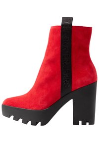 Botín de ante rojo hasta el tobillo con plataforma negra gruesa y una correa vertical negra etiquetada "Calvin Klein Jeans" en el lateral.