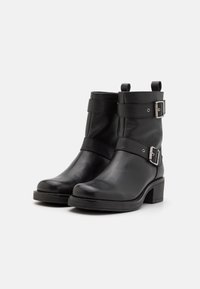 Black ankle boots made of textured leather, featuring two adjustable straps with silver buckles and a low stacked heel. Flat sole design.