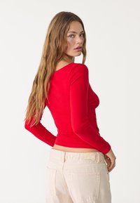 Rode lange mouw fitted top met geplooide details aan de voorkant, gecombineerd met hooggetailleerde lichtbeige jeans met achterzakken.