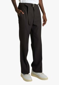 Pantaloni neri a gamba larga, con cintura in tessuto e tasche laterali, abbinati a sneaker bianche. Tessuto liscio e design moderno.