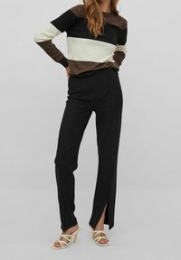 Randig tröja i svart, brunt och elfenben, kombinerad med högmidjade svarta byxor med framklippsöppningar, kompletterad med beige klacksandaler.