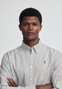 Kariertes Hemd mit feinen blauen und weißen Streifen, Knopfverschluss vorne und kleinem gestickten Logo auf der Brust. Baumwollstoff mit glatter Textur.