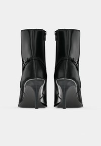 Μαύρα γυναικεία μποτάκια με τακούνι και λείο δερμάτινο φινίρισμα, με φερμουάρ στο πλάι και διακοσμητικό λουράκι κοντά στον αστράγαλο, με κυρτή σιλουέτα.