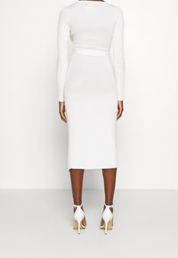 Abito bianco a coste con maniche lunghe, forma aderente e lunghezza midi. Abbinato a sandali bianchi con tacco alto. Design e texture senza cuciture.