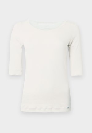 Chemise blanche côtelée avec manches trois-quarts, un large col et un ourlet légèrement arrondi. Comprend un petit logo en bas à gauche.