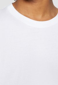 Biała bawełniana koszulka z okrągłym dekoltem, gładką fakturą i krótkim rękawem, charakteryzująca się prostym, nieskomplikowanym wzorem.