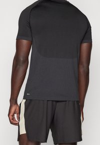 Sort atletisk T-shirt med struktureret design, korte ærmer og tætsiddende pasform. Kombineret med sorte shorts med cremefarvede side-striber.