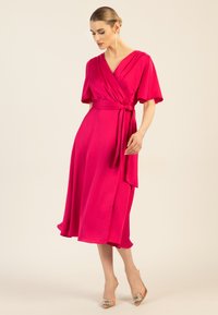 Fuchsia Wickelkleid mit kurzen Ärmeln, einem Bindegürtel und einem fließenden Rock, der unter das Knie fällt. Glattes Material mit sanftem Glanz.