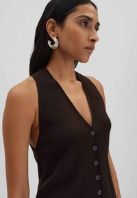 Blusa senza maniche marrone con scollatura a V profonda, caratterizzata da cinque bottoni neri lungo il davanti e una finitura liscia e testurizzata.