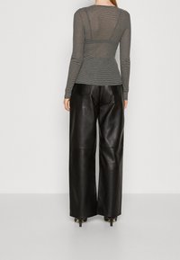 Černobíle pruhovaný top s dlouhým rukávem a přiléhavým střihem, ve spojení s černými koženými kalhotami se širokými nohavicemi, které mají hladkou texturu a jemný lesk.