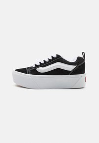 Must mustade sneakers valgete aktsentidega, paks valge tallaga, lipsudega disain ja eristuv külgtriip.