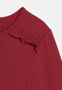 Rippentop in Maroon mit Rundhalsausschnitt und gerafften Akzenten an den Schultern, aus einem weichen, strukturierten Stoff gefertigt.