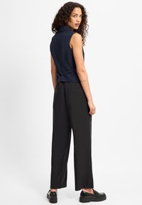 Navy gestreifte ärmellose Bluse mit hohem Kragen und rückseitiger Bindefunktion, kombiniert mit schwarzen weit geschnittenen Hosen und schwarzen Plateau-Schuhen.