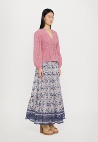 Rot-weißer gestreifter Oberteil mit Rüschendetails, kombiniert mit einem fließenden, floral bedruckten Maxirock in Blau und Weiß. Holz-Plateauschuhe runden den Look ab.