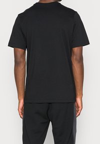 Musta puuvillapaita lyhyillä hihoilla ja pyöreällä kaula-aukolla. Sujuva rakenne, rento istuvuus, eikä näkyviä logoja tai graafisia kuvioita.