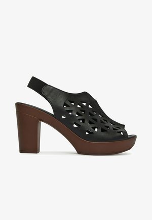 Schwarze Slingback-Sandale aus Leder mit geometrischen Ausschnitten, brauner Plateau-Sohle und Blockabsatz.