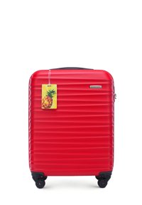 Red hard-shell suitcase with horizontal ridges, a top handle, black wheels, and a pineapple-shaped luggage tag attached.