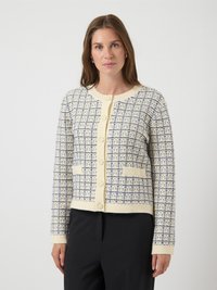 Γυναίκα που φοράει κρεμ και ναυτικές ριγέ πλέκτες κάρντιγκ με κουμπιά και δύο μπροστινές τσέπες, συνδυασμένο με μαύρο παντελόνι, σε λευκό φόντο.