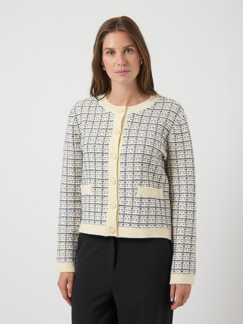 Γυναίκα που φοράει κρεμ και ναυτικές ριγέ πλέκτες κάρντιγκ με κουμπιά και δύο μπροστινές τσέπες, συνδυασμένο με μαύρο παντελόνι, σε λευκό φόντο.