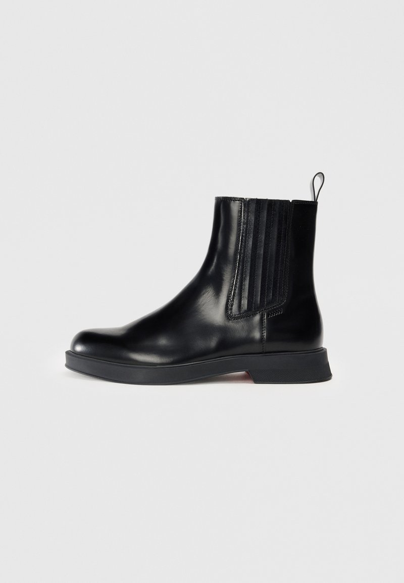 Botte en cuir noir mi-mollet avec des panneaux élastiques sur les côtés, bout rond, petit talon bloc et languette. Présente une texture lisse et un design épuré.