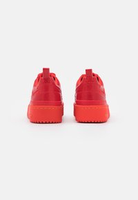 Red sneakers with textured upper, padded collar, and pull tabs. Thick, solid red sole with yellow stitching detail.