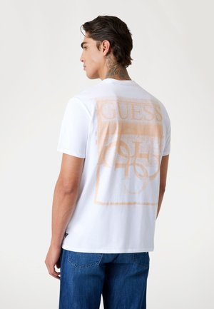 Tricou alb din bumbac cu un imprimeu mare de piersică pe spate, având cuvântul "GUESS" și modele circulare, mâneci scurte, de tip crew neck.