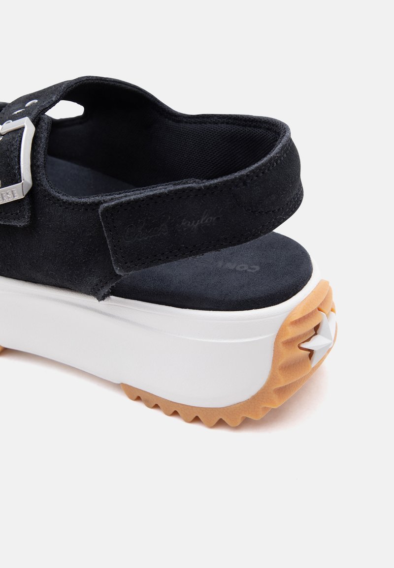 Schwarze Plateau-Sandale aus Wildleder mit verstellbarem Riemen, silberner Schnalle, gepolsterter Innensohle und weißer Sohle mit strukturiertem, hellbraunem Außensohle und Stern-Detail.