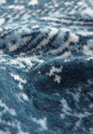 Strickstoff in verschiedenen Blautönen mit weißen geometrischen Mustern; weiche Textur mit sichtbaren Fasern und leicht gefaltetem Aussehen.