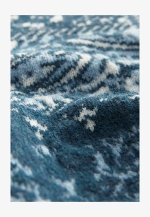 Strikket stof i nuancer af blå med hvide geometriske mønstre; blød tekstur med synlige fibre og en let foldet udseende.